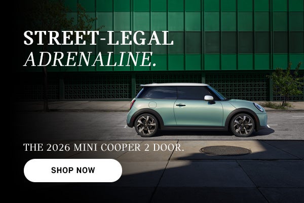 Un MINI Cooper rojo de cuatro puertas circulando por una calle de la ciudad, con un efecto de desenfoque de movimiento al fondo y un texto publicitario que promociona el modelo de 2026.