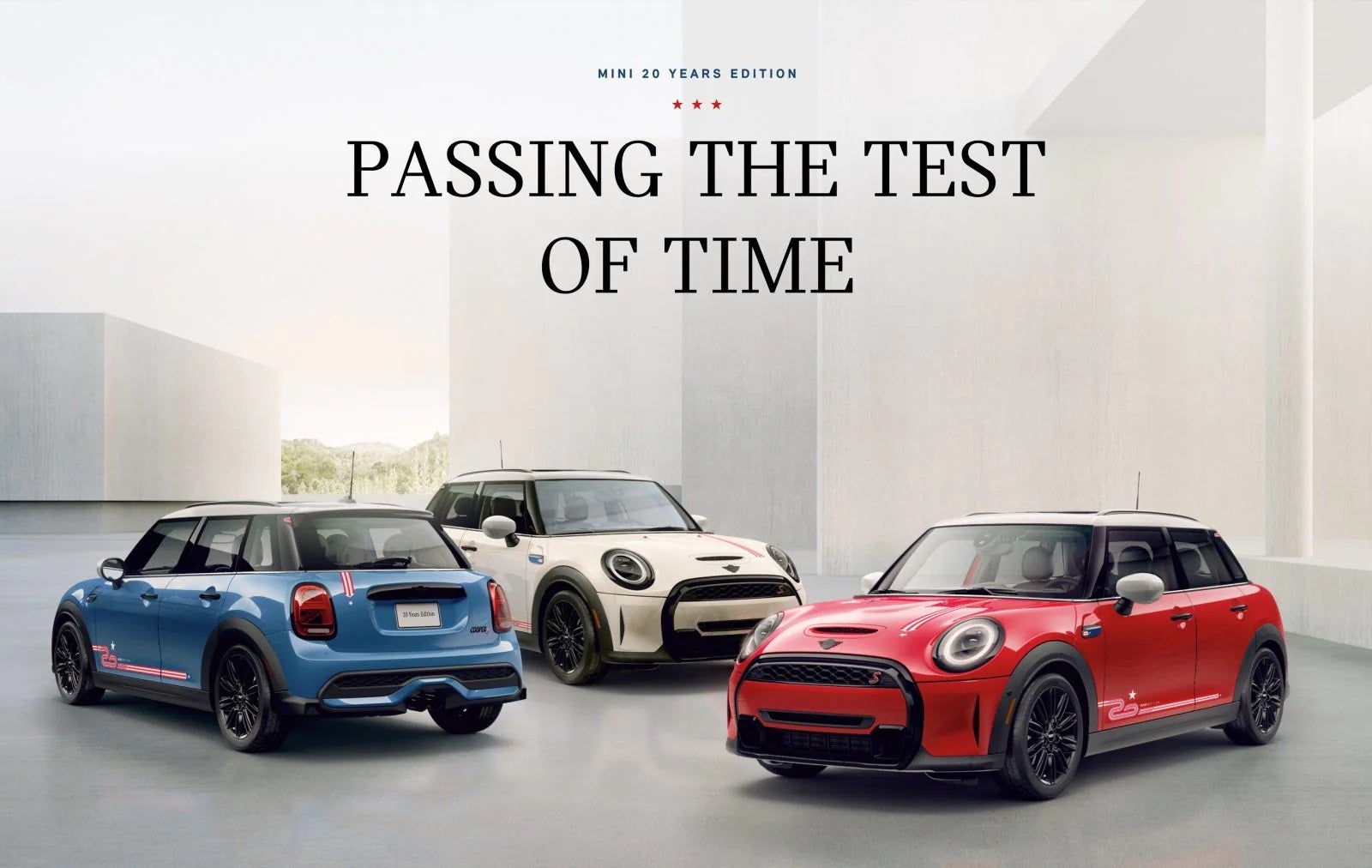 Tres MINI Edición 20 Años en azul, blanco y rojo, aparcados uno al lado del otro sobre una superficie gris con edificios cuadrados blancos de fondo. | MINI of Sterling en Sterling VA