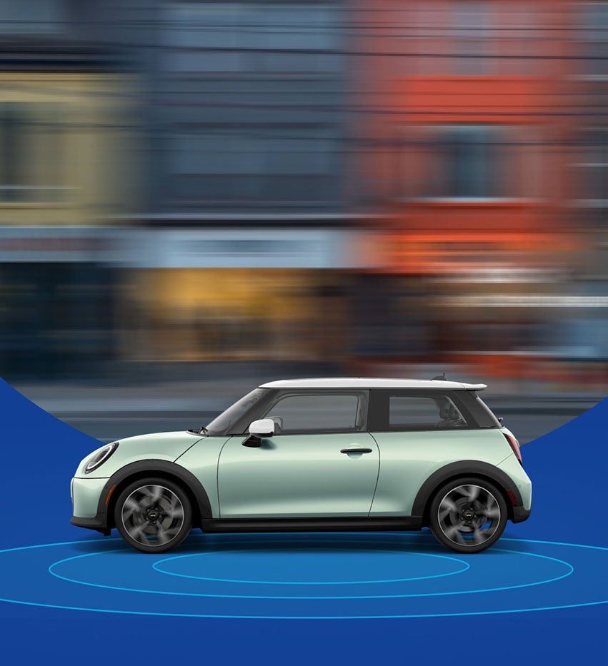 Vista lateral de un Mini Cooper Hardtop 2 Puertas con una calle de la ciudad difuminada al fondo y anillos azules debajo.