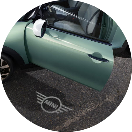 Un MINI Cooper S 2 Puertas aparcado con la puerta del conductor abierta para mostrar la proyección del logotipo MINI sobre el hormigón que hay debajo.