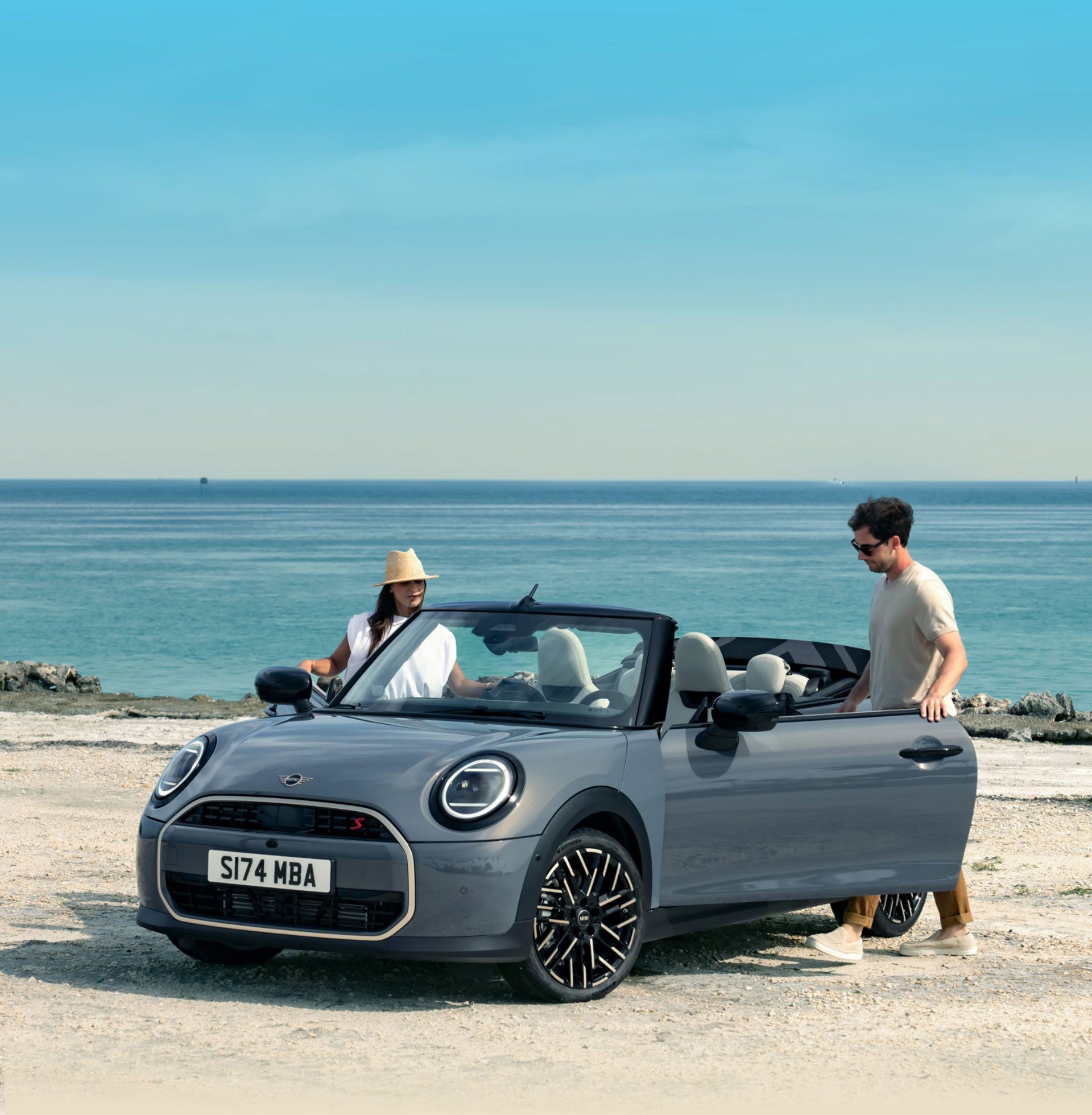 Descapotable aparcado en una playa con dos conductores subiendo a él.