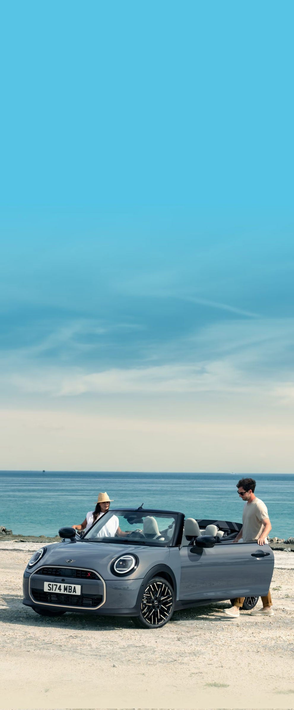 Descapotable aparcado en una playa con dos conductores subiendo a él.