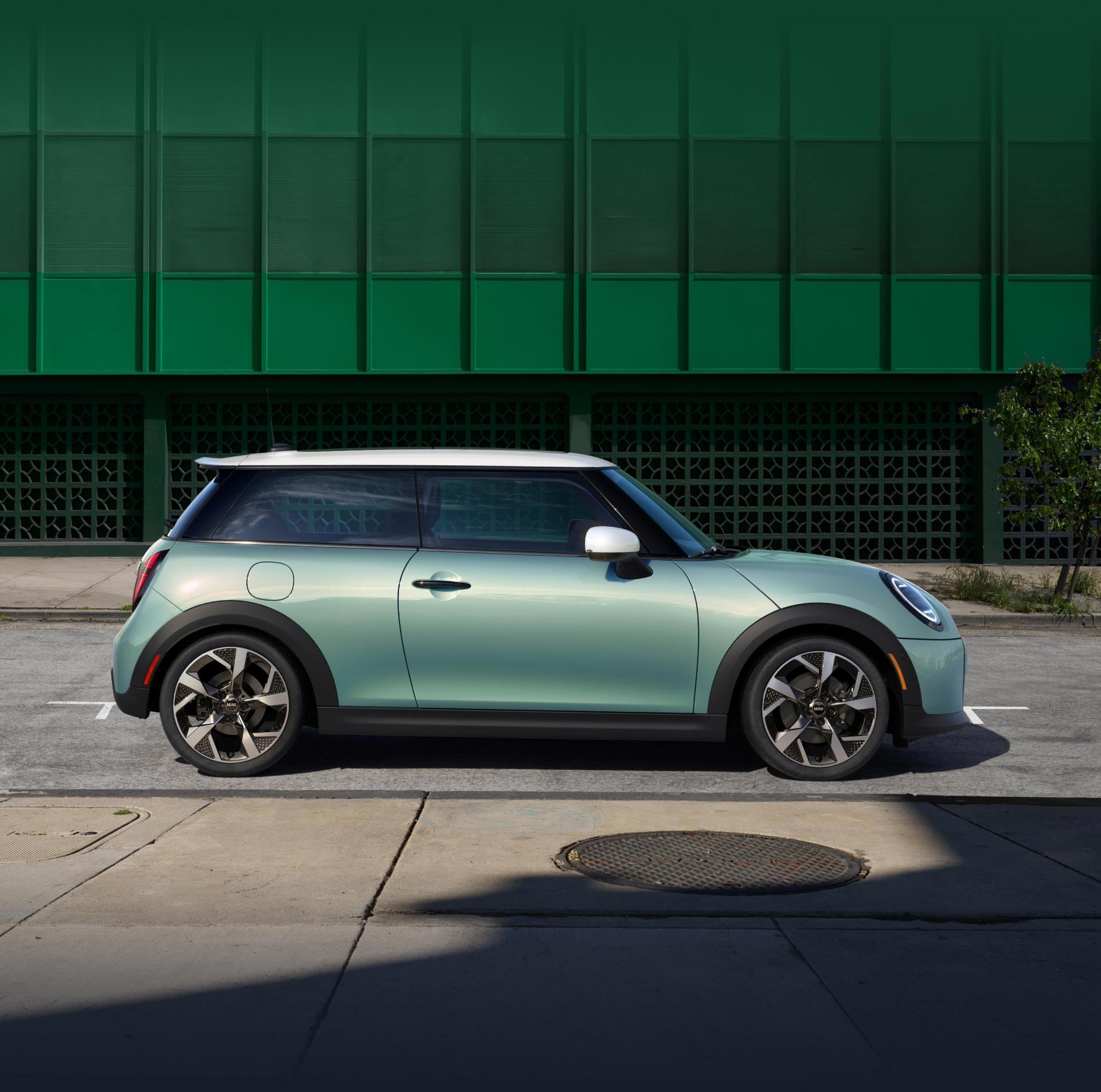 Vista lateral de un MINI Cooper S 2 Puertas en Ocean Wave Green Metallic aparcado en paralelo contra una pared verde.