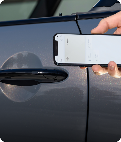 Una mano sostiene un smartphone abierto a la aplicación MINI con un volante de fondo.