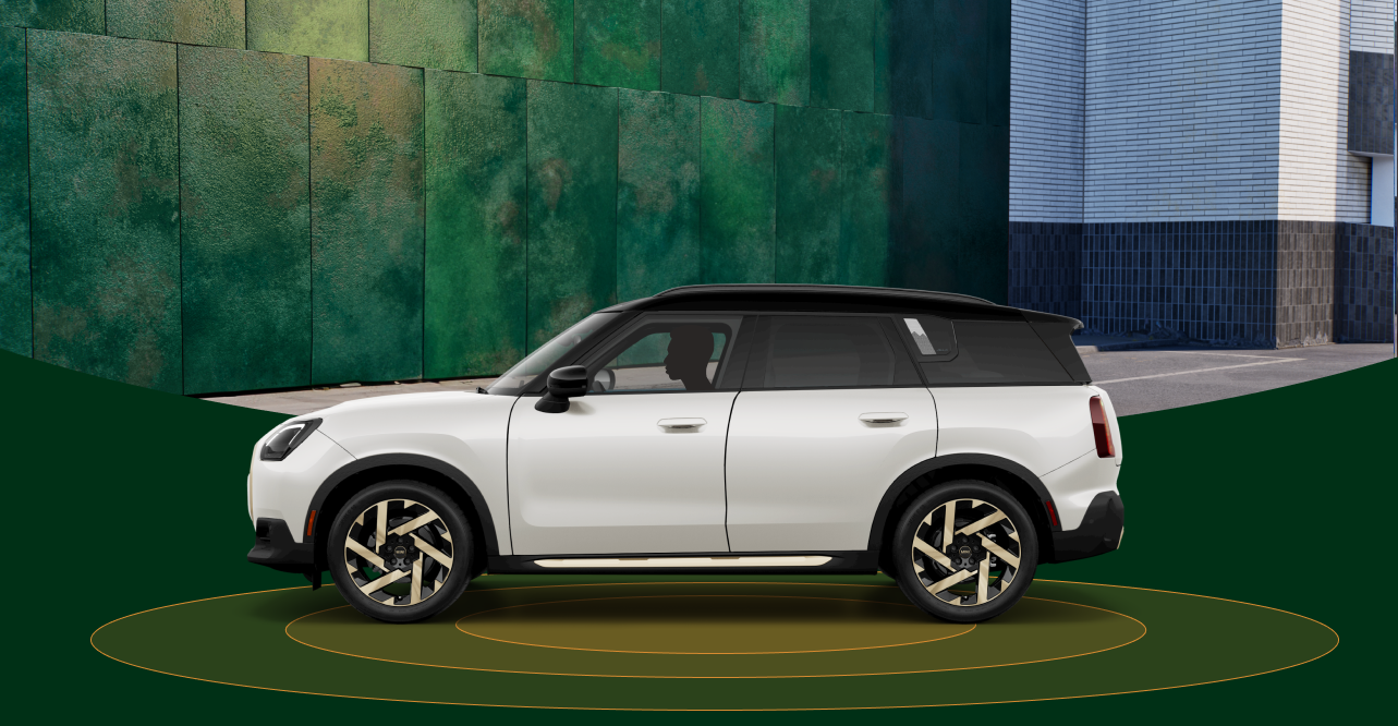 Vista lateral de un MINI Countryman SE ALL4 de 2025 con anillos naranjas debajo sobre un fondo urbano difuminado.