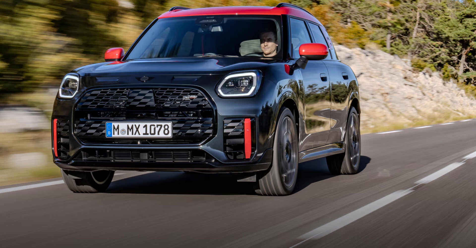Vista frontal de un MINI JCW Countryman ALL4 circulando por una carretera con fondo borroso.