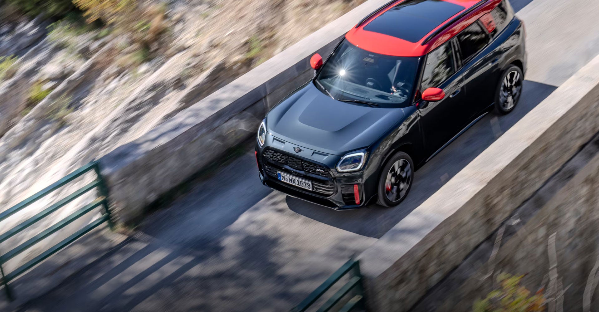Vista aérea del MINI JCW Countryman ALL4 circulando por un puente de cemento con rocas debajo. 