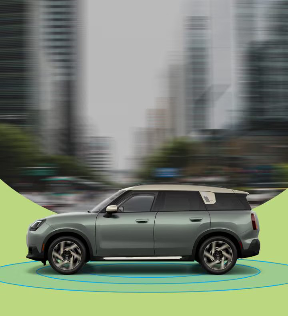 La vista lateral de un MINI Countryman S ALL4 de 2025 con una calle urbana borrosa de fondo y anillos azules debajo.