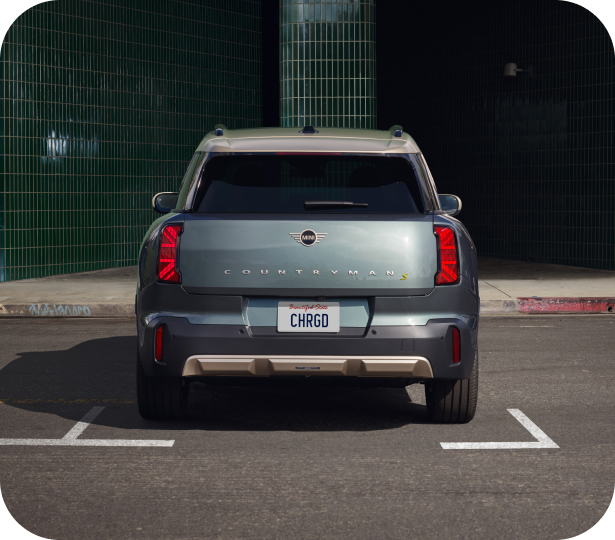 Vista frontal de tres cuartos de un vehículo eléctrico MINI aparcado sobre una superficie adoquinada en una plaza de aparcamiento frente a un escaparate en un entorno urbano.