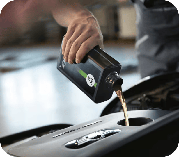 Primer plano de una mano vertiendo aceite de motor en un motor con el fondo difuminado.
