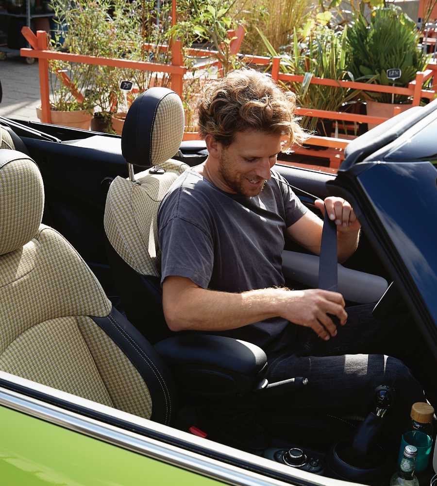 Hombre abrochándose el cinturón de seguridad en un MINI descapotable amarillo chillón