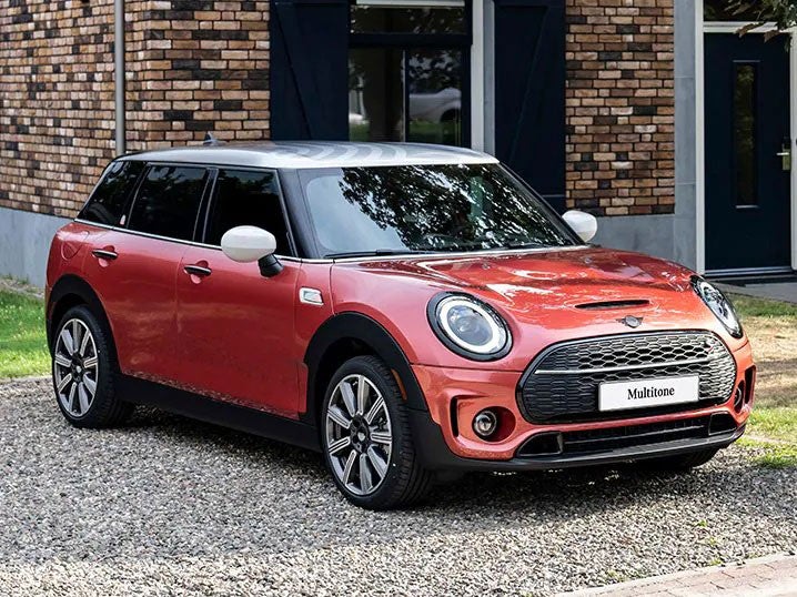 Vista frontal de tres cuartos de un MINI Clubman Multitone Edition en Rojo Coral aparcado delante de un edificio de ladrillo marrón.