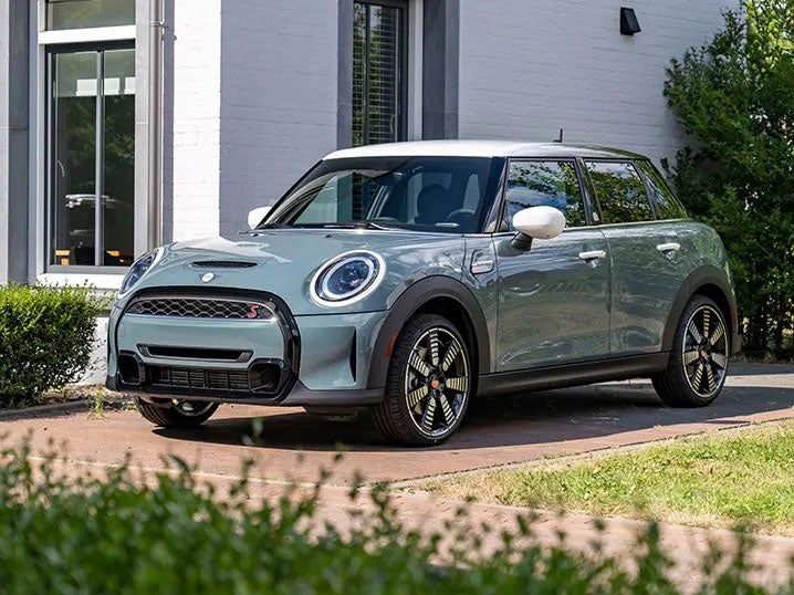 Vista frontal de tres cuartos de un MINI Hardtop 4 Door Multitone Edition en Sage Green aparcado delante de un edificio blanco.
